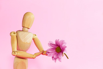 yellow wooden mannequin holding a pink chrysanthemum flower