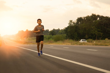 Obraz premium a boy comes to jogging in the evening on the public road on a holiday with the orange light of the sun coming from behind, leisure activities that make the body healthy