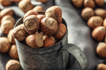 Close up of a vintage metallic mug full of hazelnuts with more nuts on a textile table cloth around it