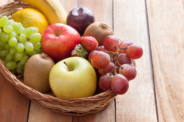 Wicker basket filled with fresh fruits against wooden background
