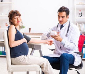 Fototapeta premium Young doctor checking pregnant woman's blood pressure