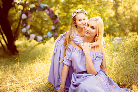 fashion outdoor photo of beautiful family look. beautiful mother with long blonde hair posing and playing with her daughter in similar lavender dresses in the park outdoor