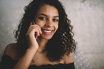 Close up portrait of cheerful dark skinned hipster girl with curly hair smiling at camera and phoning, technology communication and people concept - happy woman calling on smartphone device