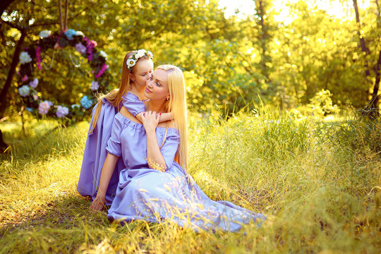 fashion outdoor photo of beautiful family look. beautiful mother with long blonde hair posing and playing with her daughter in similar lavender dresses in the park outdoor