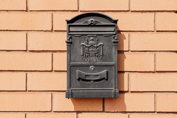 black metal mailbox with patterns on a brick wall