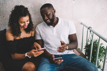 Cheerful male and female friends using cellphone device for online messaging discussing funny...
