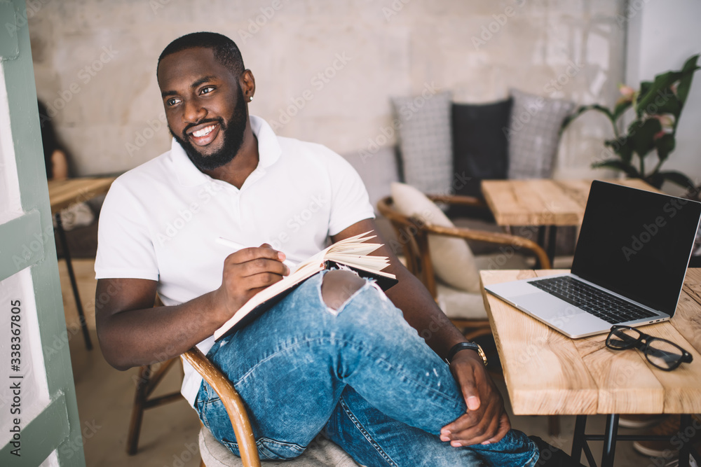 Poster happy dark skinned student studying with education textbook sitting near table with blank laptop and