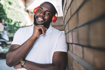 Half length portrait of dark skinned man excited with sound and loud music in modern red headphones...