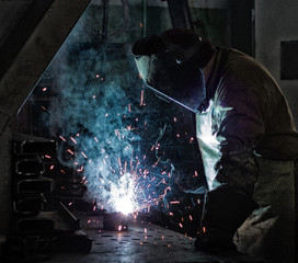 Welder at the factory welds metal parts, welding and sparks, dirty production, harmfulness