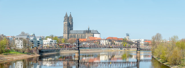 Panoramic cityscape of old railway metal rusty bridge over Elbe river in downtown of Magdeburg and cathedral at early Spring, Germany, sunny day, blue sky - obrazy, fototapety, plakaty