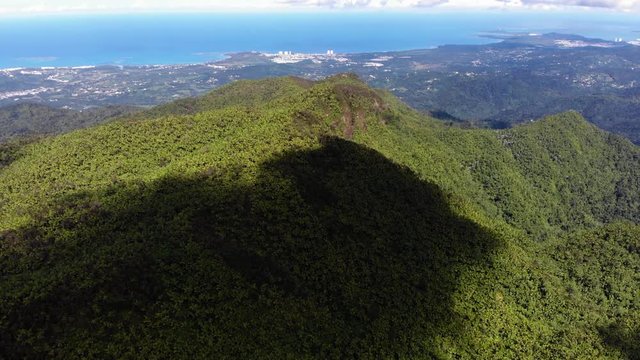 Huge shadow cast over mountain covered in sense forest with coastline and city