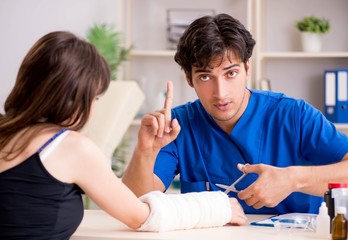 Young woman with bandaged arm visiting male doctor traumotologis