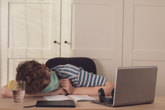 A bored teenage boy in a protective face mask  learns at his desk in his room.Distance learning because of the epidemic coronavirus