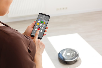 Hand controlling romote of robotic vacuum on wood laminate floor.