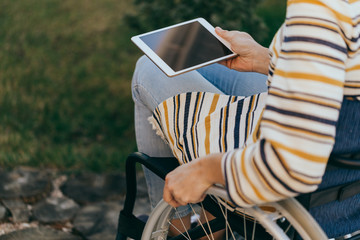 Fashionably dressed woman in a wheelchair with a modern tablet in hand walks on the street.