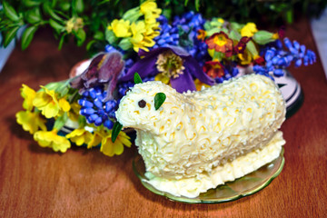 Easter lamb with butter on a background of colorful flowers on a wooden table.