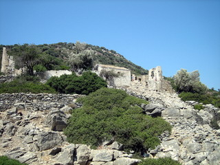 Stone ruins of an ancient building on the slope of a rocky hill, overgrown with green dense vegetation, in good weather.