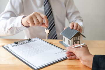 Real estate agent broker hand over the house key to the new owner after completing the signing according to agreement renting a house and buy house insurance Home insurance concept