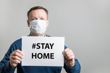 Adult man in protective medical mask holding white blank for text - STAY HOME. Covid-19. Quarantine concept. Coronavirus prevention.