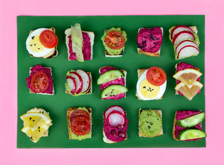 set of different bruschetta sandwiches with beet hummus, guacamole, different vegetables. vegetarian helsifood concept. summer snack. food patern on green background
