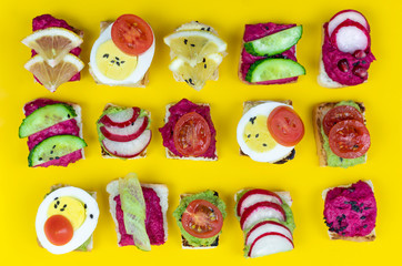 set of different bruschetta sandwiches with beet hummus, guacamole, different vegetables. vegetarian helsifood concept. summer snack. food patern on yellow background