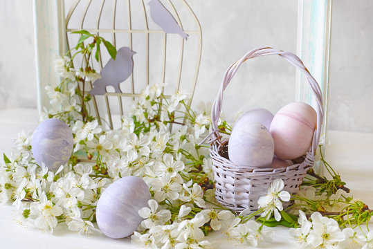 Tender Easter photo with branches of blooming cherry and colored eggs on a white wooden background.