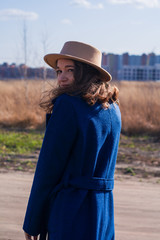 Young girl with beige hat and in blue coat walks early spring in field. Fashion, style, emotions.