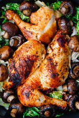 Top view of roasted chicken legs and breasts with fresh salad and mushrooms