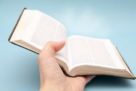 Hand With An Open Bible With Rays Of Light On A Blue Background