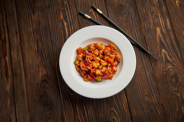 Chinese food, kung pao chicken in white plate with chopsticks on wooden table, top view and copy space