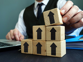 Growth business concept. Businessman makes ladder of success from blocks with arrows.