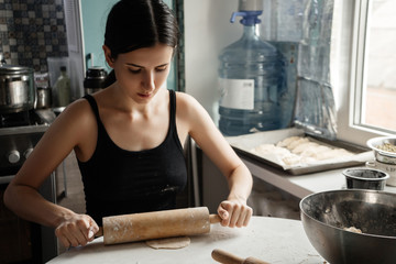 Russian woman beatifull brunette kneading bread dough with rolling pin on kitchen table. Homemade baking.