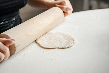 Close up on hand of unknown caucasian woman female girl making bread pastry knead the dough kneading on the kitchen table at home top view using rolling pin