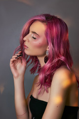 Fototapeta premium Art beauty portrait of a woman with pink hair, creative coloring. Bright colored highlights and shadows on the face, a girl with jewelry. Dyed hair in the wind