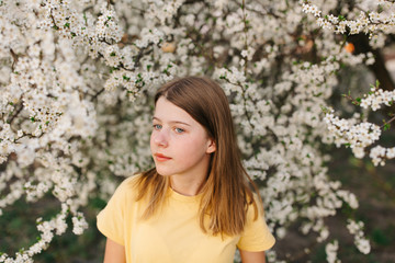 portrait of sad young woman in protective medical face mask with flowers near blooming tree in spring time. Coronavirus protection. epidemic of coronavirus. the aroma a tree in the garden on a spring