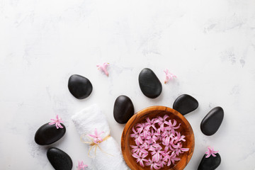 Obraz na płótnie Canvas Beauty, spa background with black massage stone and flowers in bowl on white table top view. Relaxation and wellness concept. Flat lay.