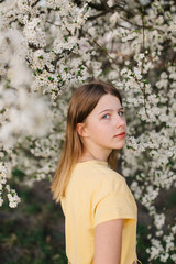 portrait of sad young woman in protective medical face mask with flowers near blooming tree in spring time. Coronavirus protection. epidemic of coronavirus. the aroma a tree in the garden on a spring