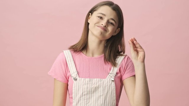 Carefree pretty brunette woman in overalls showing blah blah blah gesture and looking at the camera over pink background