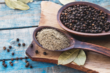 Ground black pepper in a spoon lies on a cutting board near the bay leaf and black pepper on a background of blue boards.