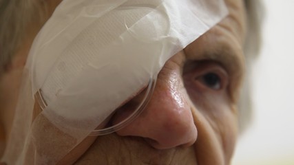 Old woman with protective eye patch after cataract surgery.