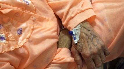 Cannula placed in the wrinkled hand of an elderly patient In hospital bed. Close up