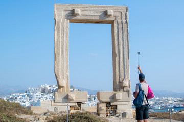 A man with a selfie stick and a mini camera attached to it is, making photos at the ancient Greek monument of Portara at the town of Naxos.