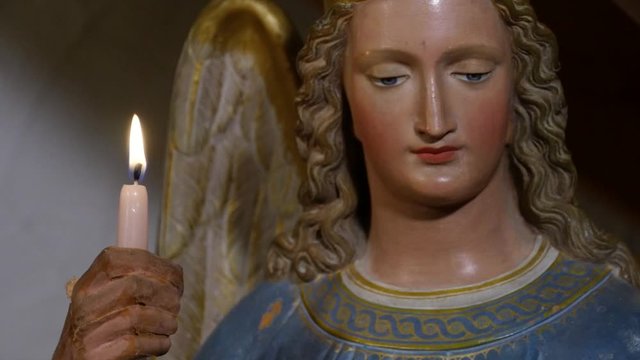 close up of a statue of an angel holding a burning candle in his hand