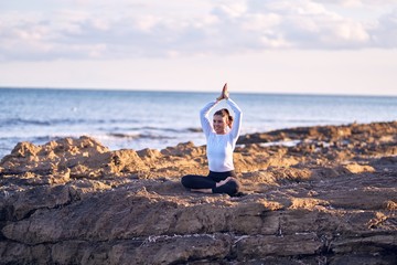 Young beautiful sportwoman smiling happy practicing yoga. Coach with smile on face teaching prayer pose at the beach