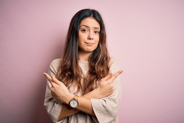 Young beautiful brunette woman wearing casual sweater standing over pink background Pointing to both sides with fingers, different direction disagree