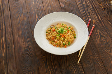 Fried rice with vegetables and beef in white plate, chopsticks on wooden background, Asian food concept, top view copy space