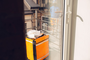 Contacless delivery service during quarantine. Man delivers food and shopping bags during isolation. Knocking at door and leaves goods until client picks it up. Safety, receiving, keeping distance.