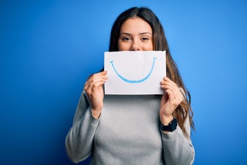 Young beautiful brunette positive woman holding card with smile emotion on mouth with a happy face standing and smiling with a confident smile showing teeth