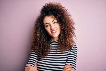 Young beautiful woman with curly hair and piercing wearing casual striped t-shirt happy face smiling with crossed arms looking at the camera. Positive person.