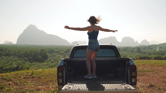 Young girl revolves around herself in the back of a pick up truck. Woman dancing and having fun on the background of mountains and wild plains
